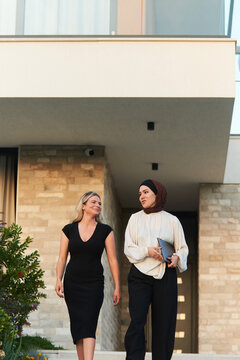 Two Professional Female Colleagues Walking and Talking Outside Modern Office Building, Business Conversation
