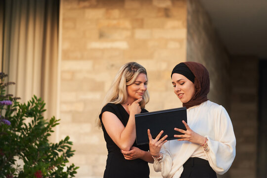 Two Professional Women Reviewing Work On A Tablet Outside Modern Office Building