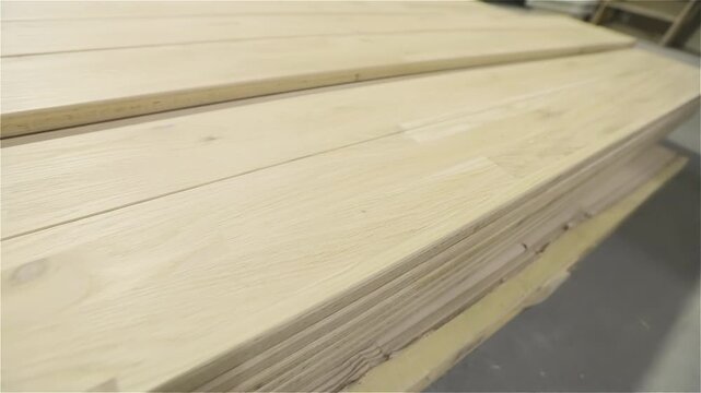Light-colored long lumber with a natural wood texture is prepared for further processing. A stack of wooden boards or a furniture panel for woodworking on the floor of a furniture factory workshop.