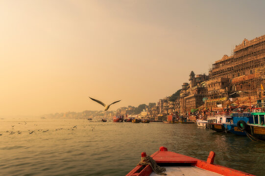 Morning glow on Varanasi ghats from boat on Ganges River, bird in flight crossing frame, warm sunrise, Banaras, India