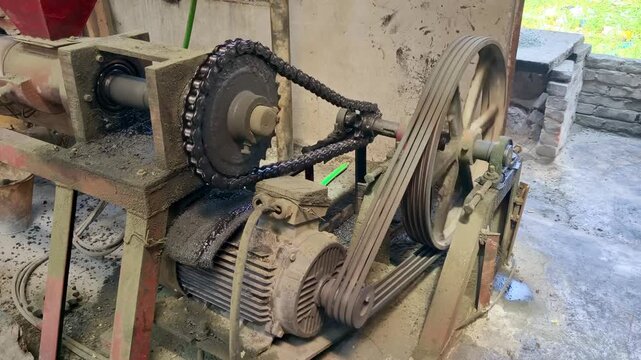 Close-up view of an active industrial electric motor operating a heavy machinery system with rotating belt pulleys and chain drives inside a manufacturing plant