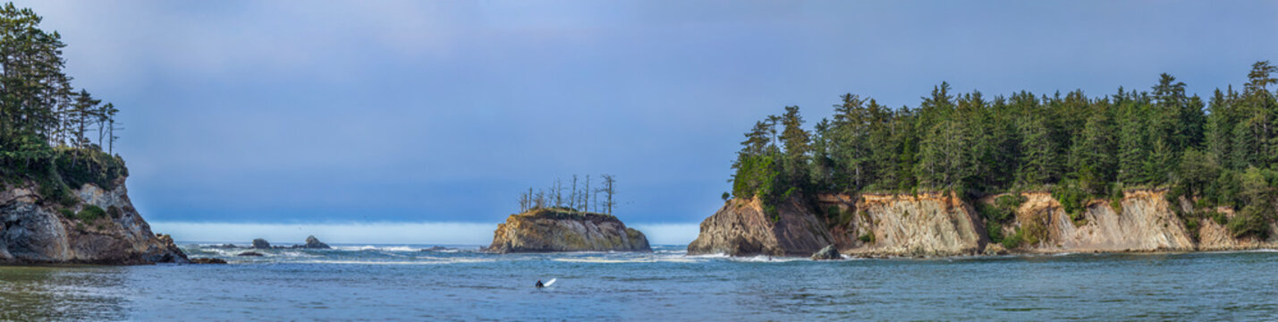 Beautiful wide panoramic view of a wild rocky ocean coast with green mountains and a distant surfer in water