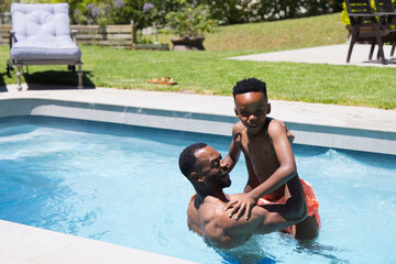 Obraz premium African American father and child playing shirtless and holding child in inground pool, copy space