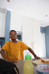 African boy in mustard tee standing with hands on kitchen counter near sandwich and water bottle © WavebreakMediaMicro
