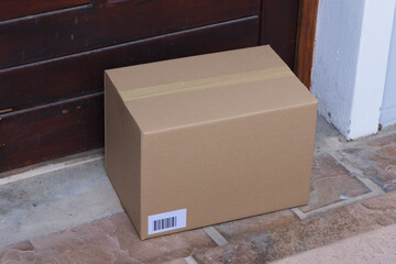 Fototapeta premium Sealed cardboard box is sitting on tiled threshold near dark wooden door with barcode label
