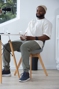 African American man wearing beanie holding white headphones speaking into boom mic in studio