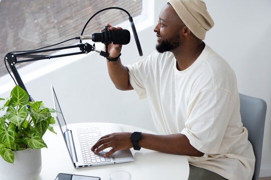 African American man in beanie recording with boom mic operating laptop at home studio, copy space
