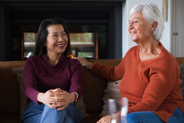 Obraz premium Asian mature woman and Senior woman sitting on sofa in living room with fireplace, pillows, smiling