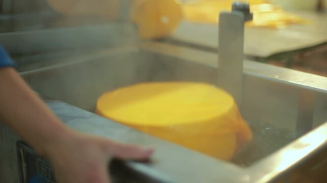 Closeup cheese wheel wax coating dairy plant. Worker dipping paraffin.