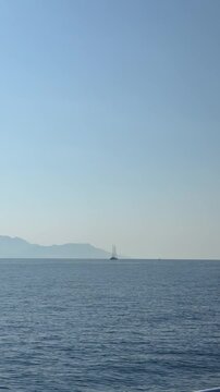 Two-masted sailing ship silhouette on calm blue sea against misty mountains, Ionian Sea, Greece