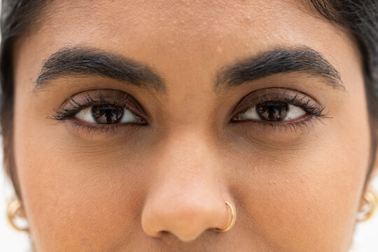 Adult Indian woman filling close-up, showing skin detail, long lashes, gold nose hoop and earrings