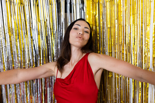 Adult female posing in red dress, puckering lips and extending arms at party booth with streamers