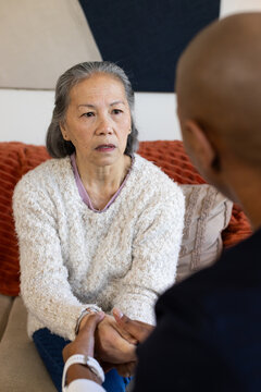 Senior woman and adult companion sitting on sofa holding hands at home with wristwatch visible
