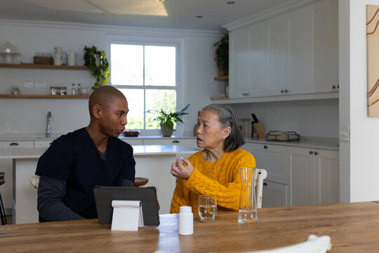 Senior Asian woman yellow-sweater holding orange med bottle, aide using tablet at home