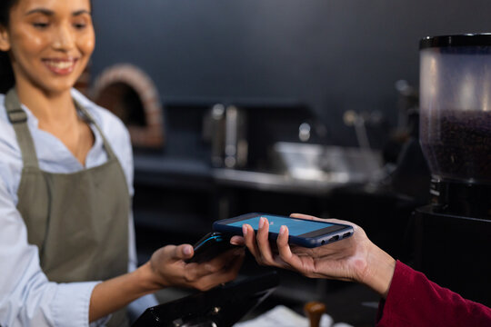 African American woman barista in olive apron tapping phone on terminal at cafe counter, copy space