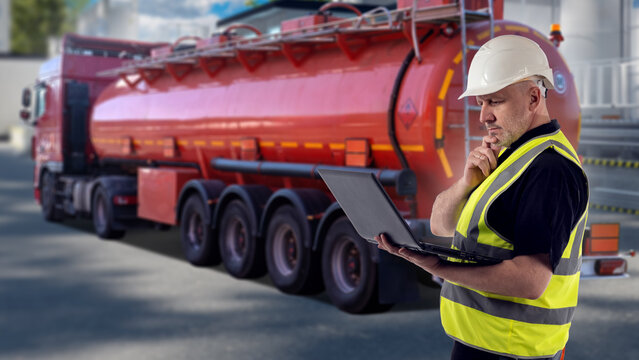 Fuel transportation, logistics manager inspects a tanker truck and checks hazardous liquid cargo delivery documents on a laptop at an industrial facility.