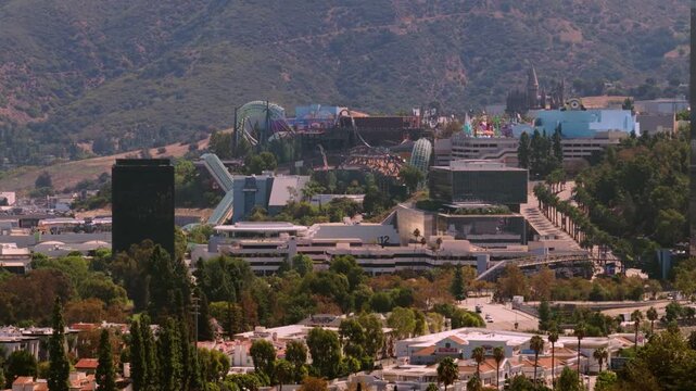 Aerial view of famous theme park rides and movie studio lot in Universal City. Los Angeles California landmark surrounded by green hills palm trees and homes. Sunny summer day over the valley.