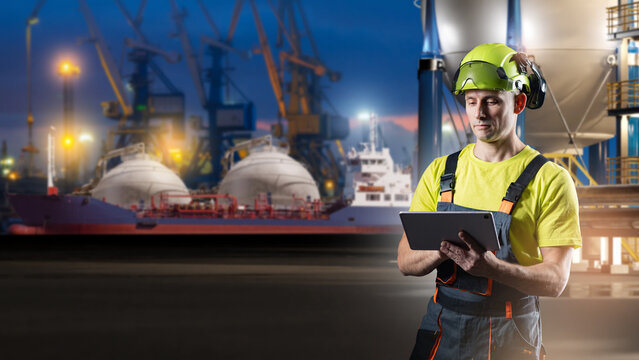 LNG shipping, port worker uses a tablet to monitor liquefied natural gas loading operations from a tanker vessel at an industrial terminal at dusk.