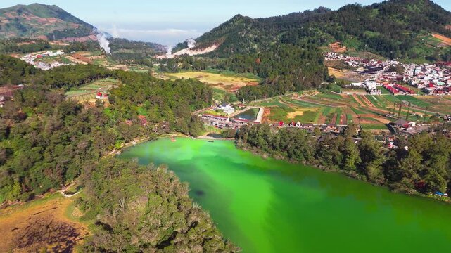 Aerial view of Telaga Warna, a vibrant green volcanic lake surrounded by lush forests and mountains in Kejajar, Central Java, Indonesia.