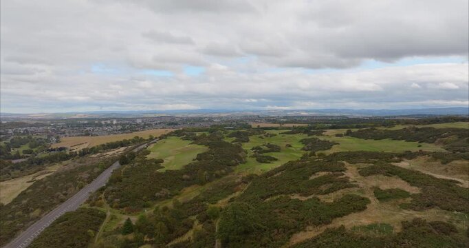 Aerial view of Braid Hills golf course featuring rolling green fairways and gorse-covered hills with the distant city skyline of Edinburgh, Scotland, United Kingdom.