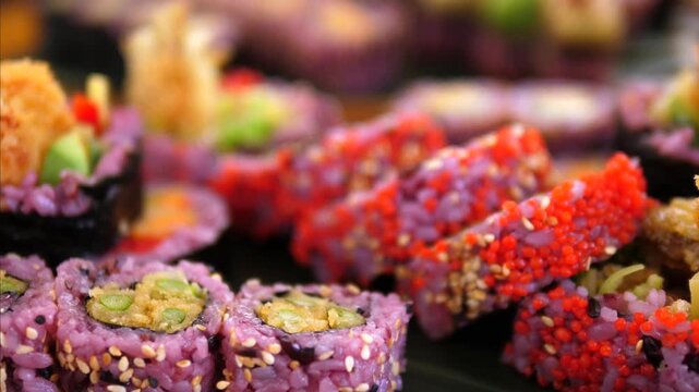 Sushi platter rests on wooden serving board in close up. Assorted rolls with purple rice, bright roe, avocado, and sesame toppings form lavish Japanese style buffet presentation with vivid texture.