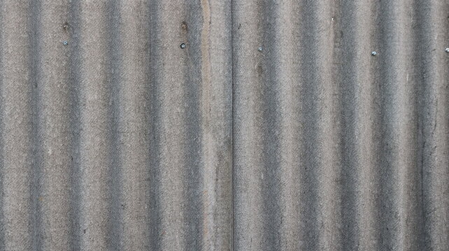 Close-up of the texture of gray corrugated roofing sheets. The surface of asbestos-cement sheets features a distinct vertical ribbed pattern, a porous texture, fine granular inclusions