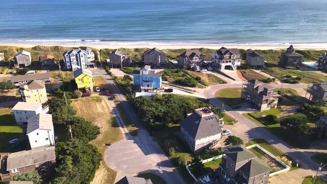 Coastal houses and residential streets spread below a retreating drone in the Outer Banks.
