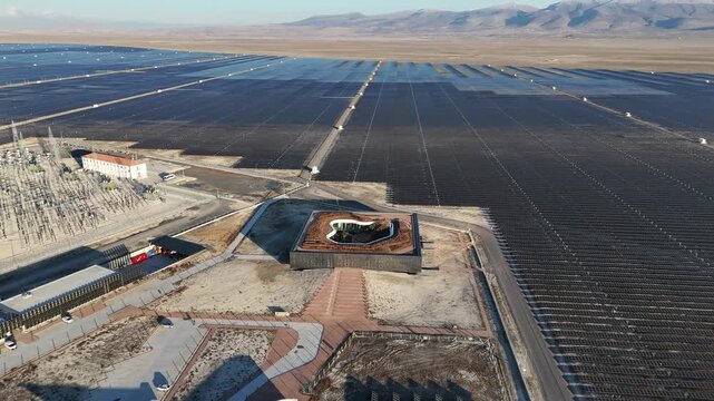 Aerial view of the vast Karapinar Solar Power Plant with rows of solar panels and a central modern building in the arid landscape of Karapinar, Konya, Turkey.