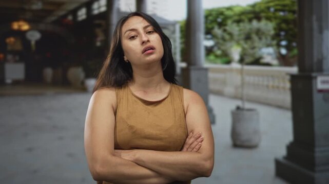 Woman with arms crossed at a building colonnade showing a skeptical pout and folded posture; annoyance defiance.