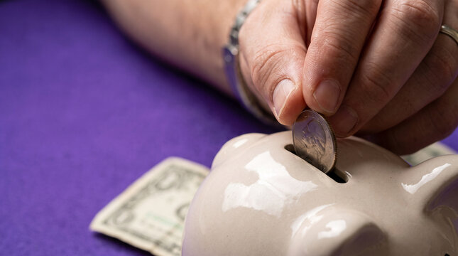 Hand placing a coin into a ceramic piggy bank on a table  