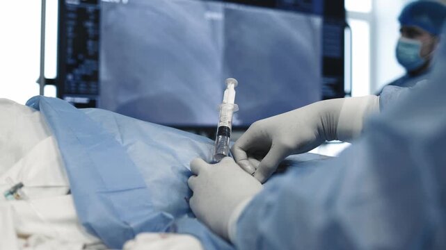 Medical specialist performing an injection through a catheter in a sterile field during angiography.
