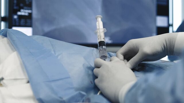 Medical specialist's hands injecting fluid through a catheter during an angiography procedure in a sterile field.
