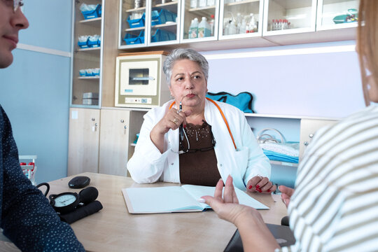 A patient is consulting with an experienced senior female doctor in her medical office, discussing their health and treatment options. The doctor listens carefully and explains the situation.