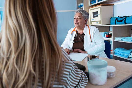 A patient is consulting with an experienced senior female doctor in her medical office, discussing their health and treatment options. The doctor listens carefully and explains the situation.