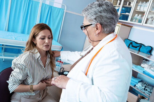 A female patient talks with an older female doctor about persistent stomach pain during a medical consultation. 