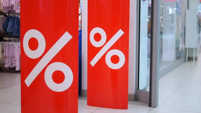 White percent symbols stand out on red sale banners beside clothing racks. Fashion store promotion highlights discounted apparel, giving shoppers clear reason to browse current retail deals.