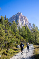 Obraz premium Two hikers on a gravel trail heading towards a massive mountain peak