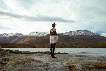 Obraz premium Woman standing on a rocky shore looking towards mountains and water in a natural landscape during daytime
