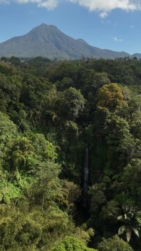 Aerial view of Baung Waterfall surrounded by lush tropical rainforest and a towering Kawi Mountain in the background in Wonosari, Malang, East Java, Indonesia.