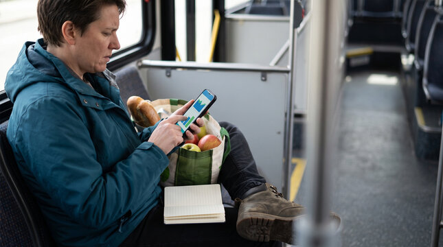 Adult woman using smartphone while sitting on bus with groceries  