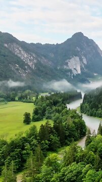 Picturesque bend of the river in the mountain valley in the morning. Majestic view of the mountain range, shrouded in light morning fog. The river meanders smoothly along the dense green forest. Natur