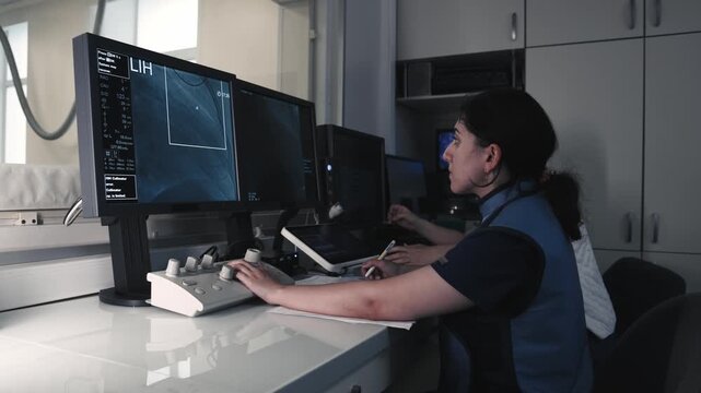 Medical specialist working at a computer workstation and monitoring angiographic images on multiple screens.
