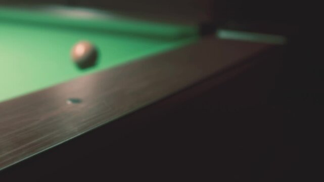 A pool table sits in a dark room. Green felt covers the table. Several balls are positioned for a game. The atmosphere feels relaxed as friends gather to play.