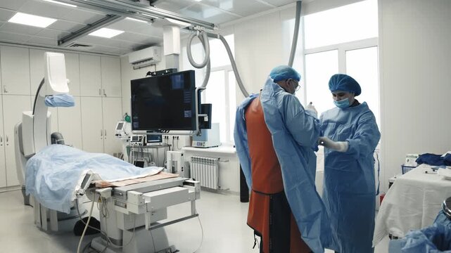Two medical specialists preparing for an interventional procedure beside a patient and angiography equipment.