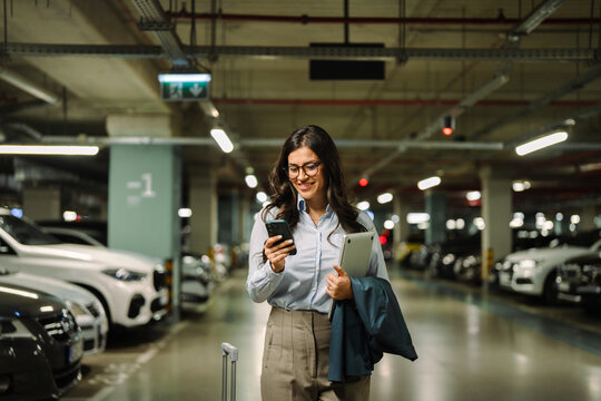 Businesswoman checking smartphone walking through parking garage