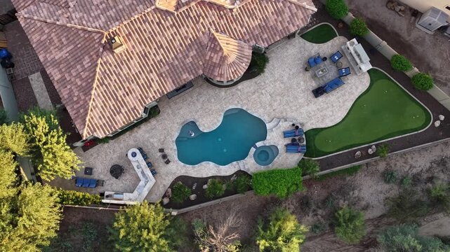 A 4k video of a desert landscaped backyard in Arizona featuring a travertine tiled pool deck, outdoor kitchen , spa and fireplace.