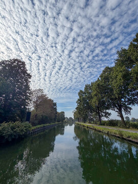 Tranquil canal with mackerel sky clouds reflecting in calm water lined by trees in Rijkevorsel, Belgi&euml;