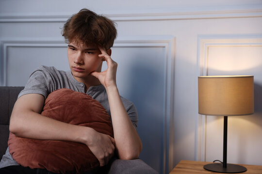Teenage boy with cushion suffering from stress at home. Space for text