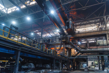 Crane spans steel factory hall above industrial machinery in pipe mill infrastructure for manufacturing. © DedMityay