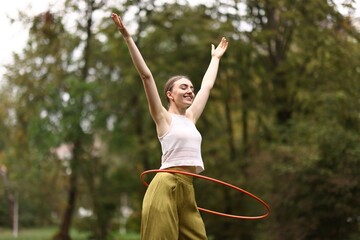 Athletic young woman exercising with hula hoop in park © New Africa